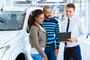 Couple reviewing car loan information while shopping for a new car at automotive dealership.